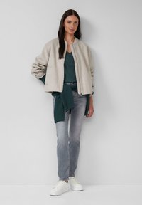 Giubbotto bomber grigio chiaro, top turchese, jeans grigi e sneakers bianche. Il giubbotto presenta una chiusura a zip e polsini a costine.