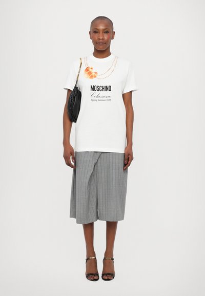 White t-shirt with black logo and croissant graphic, paired with gray striped culottes and black strappy sandals. Black shoulder bag.
