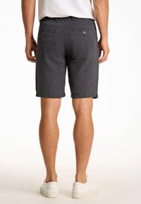 Shorts gris à rayures avec une coupe ajustée. Comprend des poches arrière avec des fermetures à bouton et des ourlets roulés. Le matériau semble respirant et texturé.