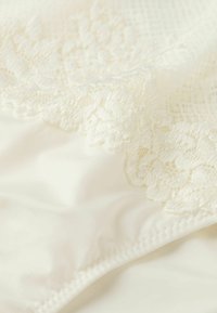 Ivory stof met delicate kantafwerking en bloemmotieven, met een zachte, gladde textuur. Het ontwerp heeft een subtiele glans en nette stiksels.