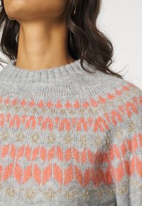 Szary sweter z dzianiny z okrągłym dekoltem, z geometrycznym wzorem w kolorze koralowym i złotymi akcentami na wysokości klatki piersiowej i ramion.