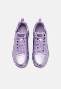 Scarpe sportive viola con una finitura metallica liscia, dotate di dettagli perforati sulla punta, interno testurizzato e lacci piatti. Marchio dello stile visibile.