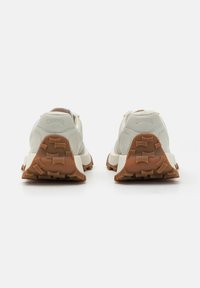 White sneakers with a textured finish, brown rubber outsole featuring a distinct tread pattern, and a subtle logo on the heel.