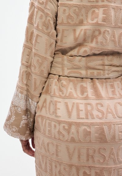 Μπεζ ρόμπα με υφή, με ανάγλυφα γράμματα "VERSACE", διακοσμητικά μοτίβα στα μανίκια και ζώνη στη μέση για ρυθμιζόμενη εφαρμογή.