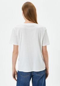 Camiseta de algodón blanca con corte recto, mangas cortas y un ajuste relajado. Presenta un escote redondeado y un diseño minimalista.