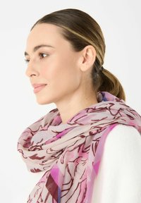 Sciarpa leggera con motivo floreale in sfumature di rosa, realizzata in un tessuto morbido con una leggerissima texture, drappeggiata elegantemente attorno al collo.