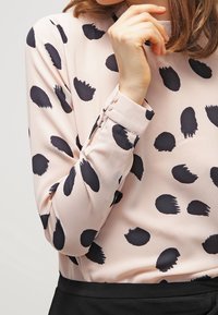 Blusa a maniche lunghe in tessuto rosa chiaro con ampi motivi a pennellate nere, dotata di polsini con bottoni e una silhouette aderente.