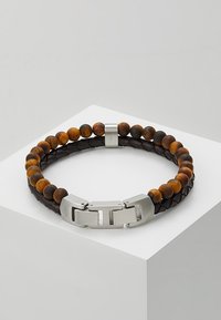 Bracciale in pelle nera intrecciata con perle rotonde in occhio di tigre, chiusura in metallo argentato, caratterizzato da una finitura liscia e texture contrastanti.