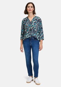 Blouse imprimée avec un décolleté en V, des manches trois-quarts et une coupe ample. Présente des motifs abstraits bleu et vert ; associé à un jean slim et des baskets blanches.