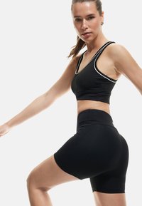 Set atletico nero composto da un top corto con bordi bianchi e pantaloni corti a vita alta. Il materiale sembra liscio, elastico e aderente.