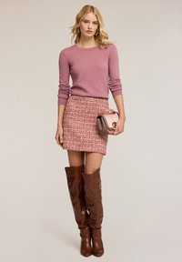 Maglione rosa aderente, gonna in tweed rosso e bianco a trama, stivali in pelle marrone fino al ginocchio e una piccola borsa rosa.