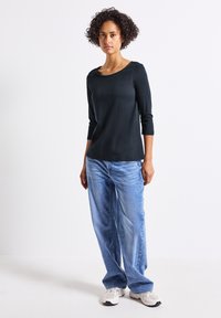 Maglietta nera a maniche lunghe con scollo tondo, abbinata a jeans azzurri larghi e scarpe da ginnastica bianche. Tessuto semplice e morbido.