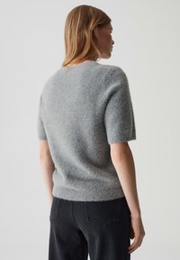 Lichtgrijze korte mouw trui met een zachte, textuurrijke afwerking en een iets losse pasvorm; gedragen met zwarte denim jeans.