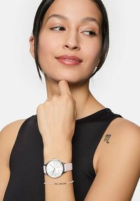 Silberne Uhr mit einem pinken Silikonarmband, rundes Ziffernblatt mit weißem Hintergrund und floralen Akzenten. Armband im Vordergrund mit Perlen.