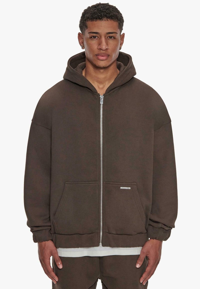 Hoodie zippé marron avec une grande capuche, poches avant et poignets côtelés. Fabriqué en tissu doux, avec une coupe décontractée et un branding minimal.