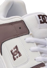White high-top sneaker with brown leather accents, textured mesh tongue, white laces, and DC logo embroidered in brown on the side.