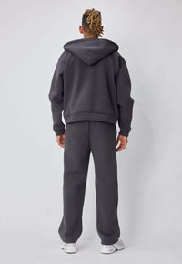 Sweat à capuche gris surdimensionné avec une large capuche, assorti à un pantalon gris assorti. Le tissu semble doux avec une texture lisse, sans motifs visibles.