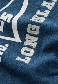 Tessuto blu con testo cucito bianco che recita "LONG ISLAND" e parte di un ampio design grafico bianco.