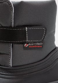 Gros plan sur une botte grise et noire avec une bride noire et une étiquette cousue portant l'inscription "ALU-Protect membrane" sur le côté.
