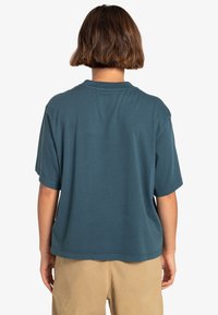 Turkusowa bawełniana koszulka o luźnym kroju, krótkich rękawach i okrągłym dekolcie. Widoczne przeszycia wzdłuż dolnej krawędzi i rękawów.