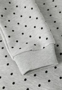 Gray sweatshirt fabric featuring a repetitive pattern of small black dots. The cuff shows a ribbed texture for added stretch.