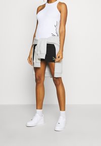 Person som bär en vit ärmlös bodysuit, svart minikjol, grå sweatshirt knuten i midjan, vita strumpor och vita sneakers, stående.