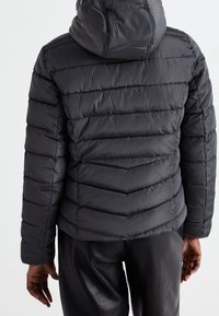 Zwarte pufferjack met een capuchon, voorzien van horizontaal doorgestikte secties. Het materiaal heeft een gladde, glanzende textuur en een aansluitende silhouette.