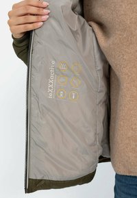 Olive green jacket with gray lining; features waterproof, breathable, and windproof indicators; smooth texture and zipped closure.