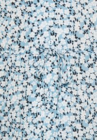 Tissu bleu clair avec de petits motifs floraux blancs et noirs, comportant une fermeture à boutons et un détail de taille nouée.