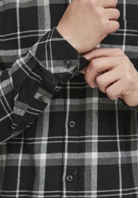 Czarna i szara koszula flanelowa w kratę. Oferuje guziki na mankietach i z przodu, ma miękką teksturę oraz dopasowany krój.