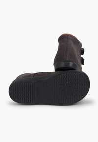 Botas de tobillo de ante gris oscuro con dos hebillas decorativas y una suela de goma texturada que presenta un patrón ondulado. La bota tiene una punta redondeada.