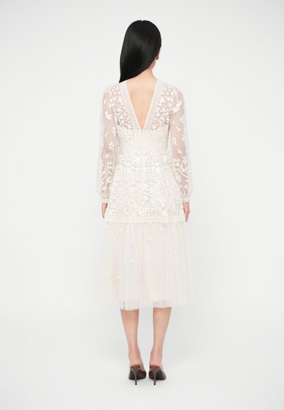 Rochie albă cu mâneci lungi, broderie florală, spate în V și fustă din tull stratificat, cu țesătură texturată și detalii delicate.