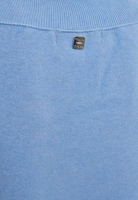 Maglione lavorato a maglia blu chiaro con scollatura a costine e una piccola etichetta metallica sul retro. Texture morbida, finitura liscia.