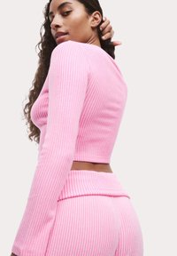 Geribbelde roze gebreide crop top met lange mouwen, die een aansluitend ontwerp laat zien. De textuur benadrukt een gladde afwerking en subtiele verticale strepen.