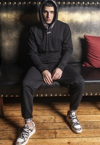 Svart huvtröja med rutigt foder, tillsammans med matchande svarta sweatpants och vita sneakers med ett rutigt mönster.