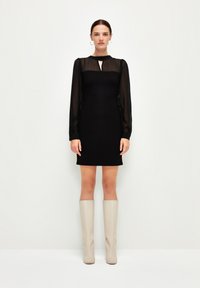Černé šaty s průhlednými dlouhými rukávy a výstřihem do tvaru klíčové dírky. Kombinované s béžovými kozačkami po kolena. Jednoduchý, elegantní silueta.