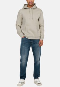 Lys grå hættejakke med snoretræk, frontlomme, parret med blå jeans og hvide sneakers med grå accenter. Simpelt, afslappet design.