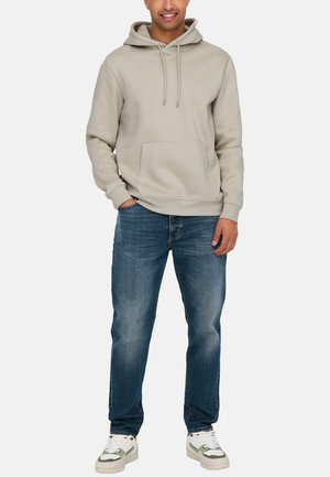 Ljusgrå hoodie med dragband, framficka, i kombination med blå jeans och vita sneakers med grå detaljer. Enkel, avslappnad design.