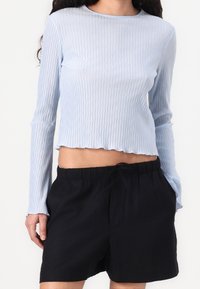 Długorękawowy, jasnoniebieski prążkowany top o krótkim kroju. W zestawie czarne szorty z troczkiem, z elastycznym pasem.