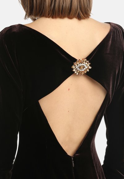 Juoda veliūro suknelė su giliu V formos nugara, kurios centre yra įspūdingas segė su skaidriais ir gintariniais akmenimis. Tiesios, prigludusios linijos.