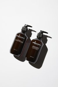 Zwei bernsteinfarbene Kunststoffflaschen mit schwarzen Pumpen. Die Etiketten enthalten in weißem Text "Handseife" und "Beruhigende Handcreme".