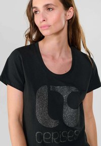 Sort bomuld T-shirt med rund halsudskæring og korte ærmer. Har et skinnende sølvglitrende logo og teksten "cerises" på forsiden.