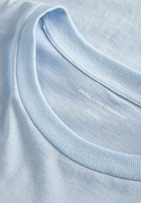 Maglietta di cotone azzurro chiaro con scollo rotondo, caratterizzata da una texture morbida e un'etichetta stampata che mostra il marchio e la taglia.