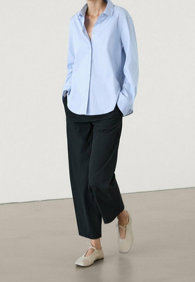 Light blue button-up shirt with a spread collar, paired with black wide-leg trousers and light gray slip-on shoes. Simple, clean design.