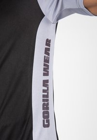 Zwart en grijs sportshirt met een gedurfde "GORILLA WEAR" print aan de zijkant in donkere letters; zacht materiaal met een normale pasvorm.