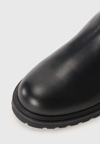 Bottine en cuir noir avec un bout arrondi, un dessus texturé et une semelle en caoutchouc noir contrastante dotée d'un cramponnage rainuré pour l'adhérence.