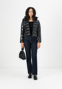 Zwarte pufferjack met een glanzende afwerking, cropped ontwerp, gecombineerd met donkerblauwe jeans en een kleine zwarte handtas. Zwarte schoenen maken de look af.