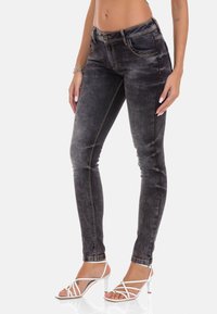 Schwarze Denim-Skinny-Jeans mit heller Verwaschung, Kontrastnähten und klassischem Fünf-Taschen-Design. Mit Knopfverschluss und Gürtelschlaufen.