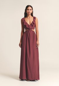 Abito maxi in tessuto bordeaux con pois bianchi, scollo a V arricciato, vita con taglio a fessura e gonna fluida. Spalline regolabili.