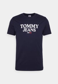 Námořnická modrá bavlněná tričko s velkým bílým nápisem "TOMMY JEANS" a malým červeným a bílým pruhem pod nápisem. Krátké rukávy, kulatý výstřih.